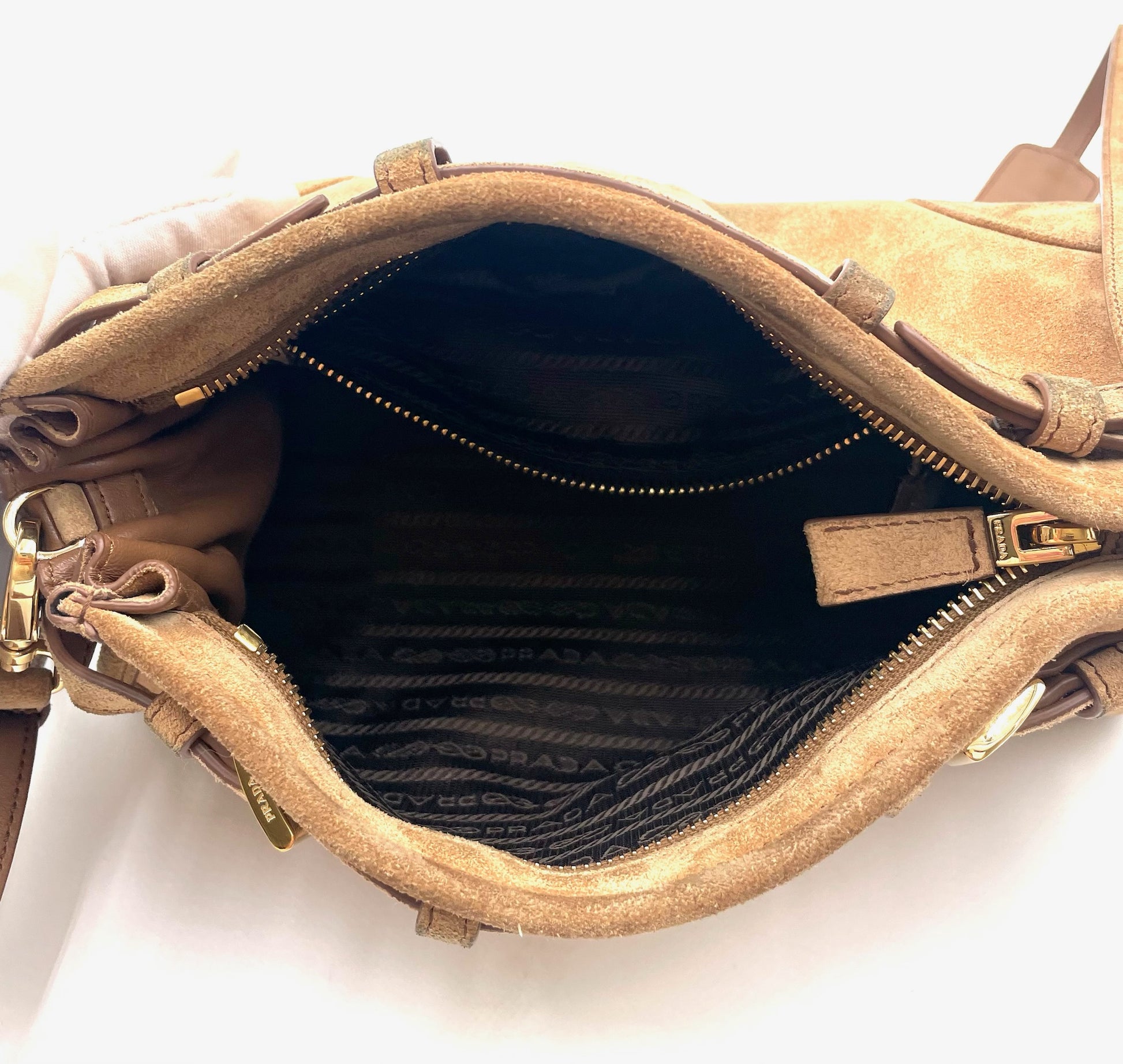 Interior of a cinnamon brown suede Prada Bonnie bag with gold hardware and logo jacquard lining.