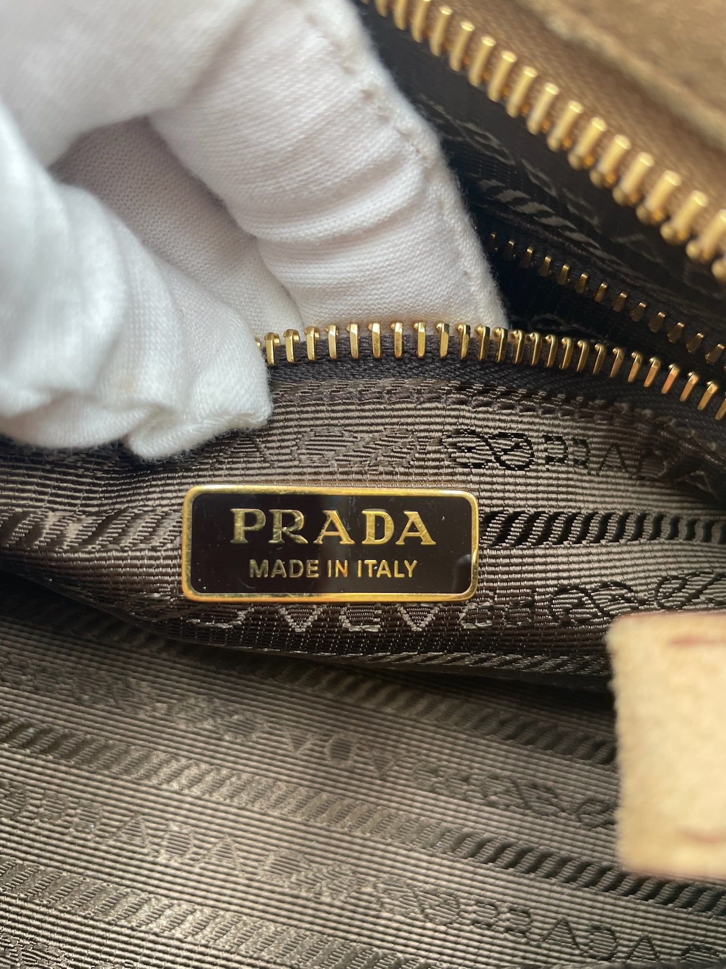 Interior of Prada cinnamon suede bag showing gold Prada Made in Italy logo plaque and brown logo jacquard lining.