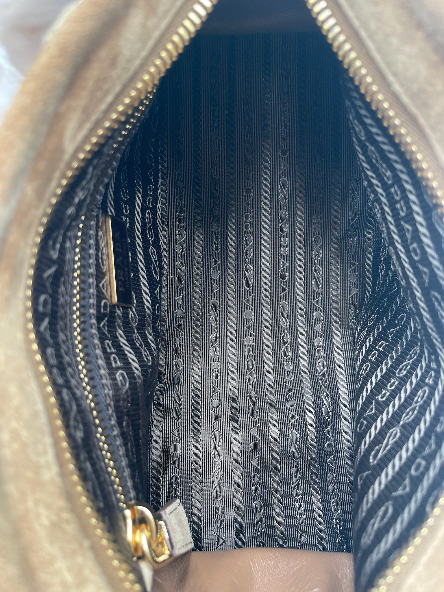 Interior of Prada Bonnie bag featuring black and white logo jacquard lining, gold zipper, and interior pocket.