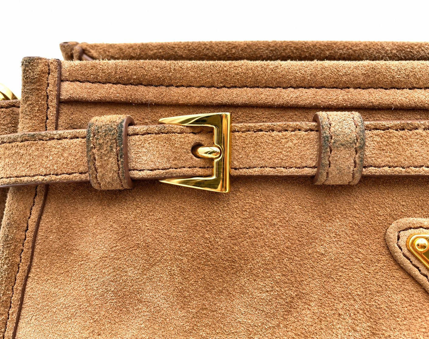 Close-up of a cinnamon brown suede Prada Bonnie bag featuring a polished gold buckle strap and visible color transfer.