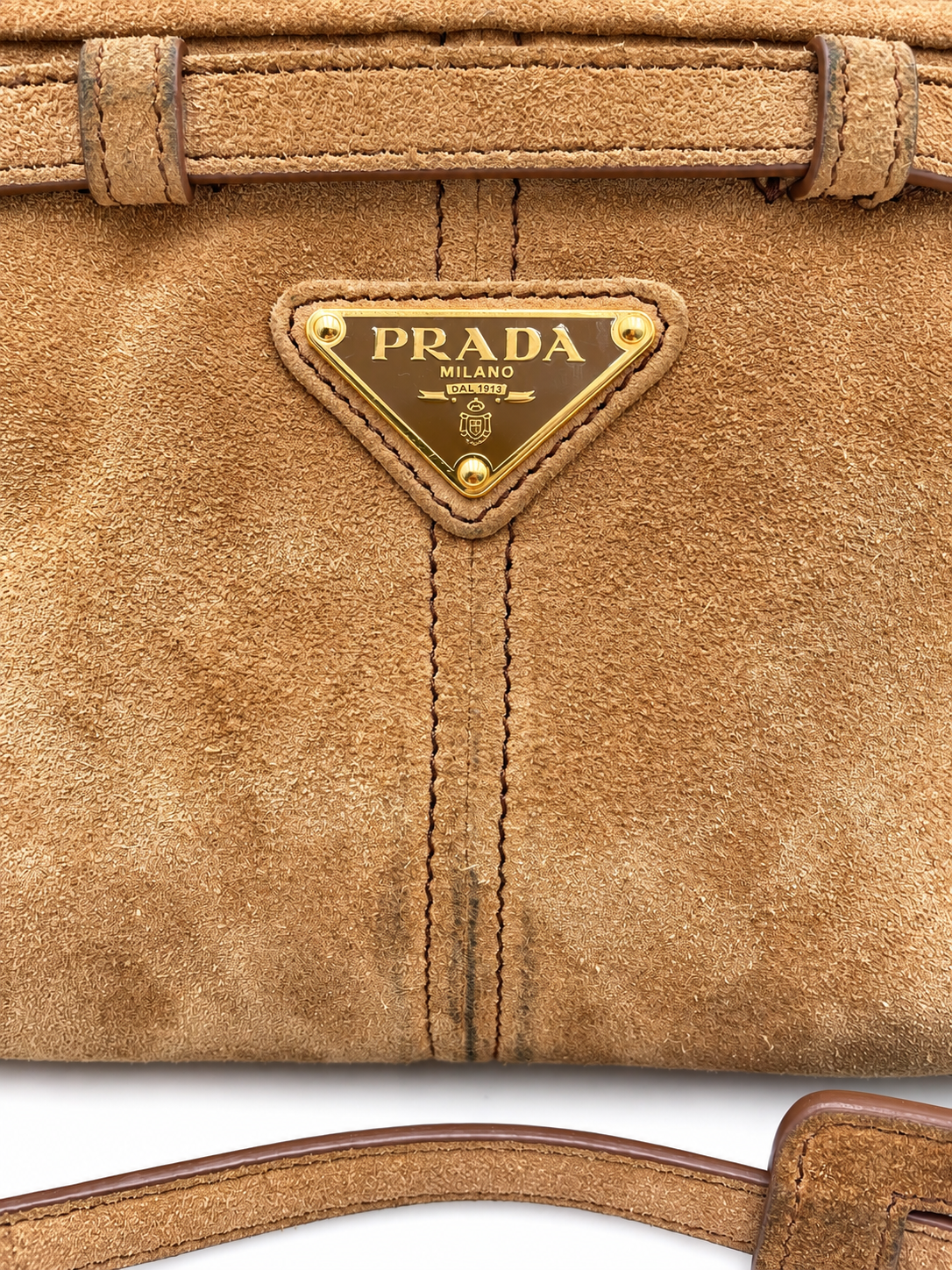Prada cinnamon brown suede shoulder bag with gold triangular logo plaque and visible color transfer.