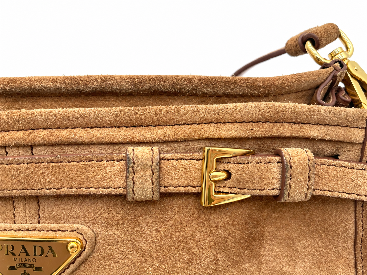 Cinnamon brown suede Prada Bonnie shoulder bag featuring gold hardware, a buckled strap detail, and a triangular logo plaque.
