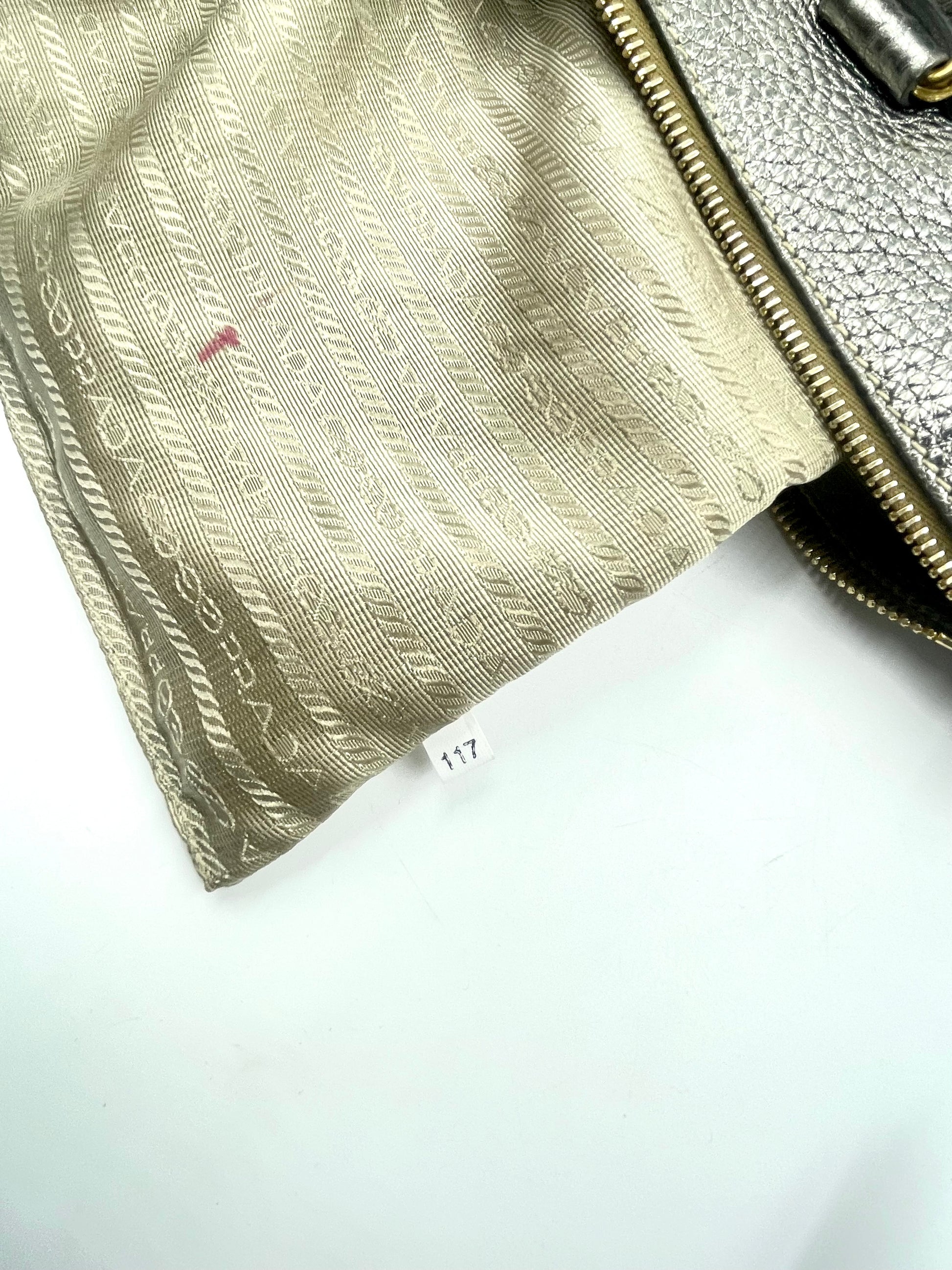 Prada metallic silver Vitello Daino tote showing textile-lined interior with ink stain.