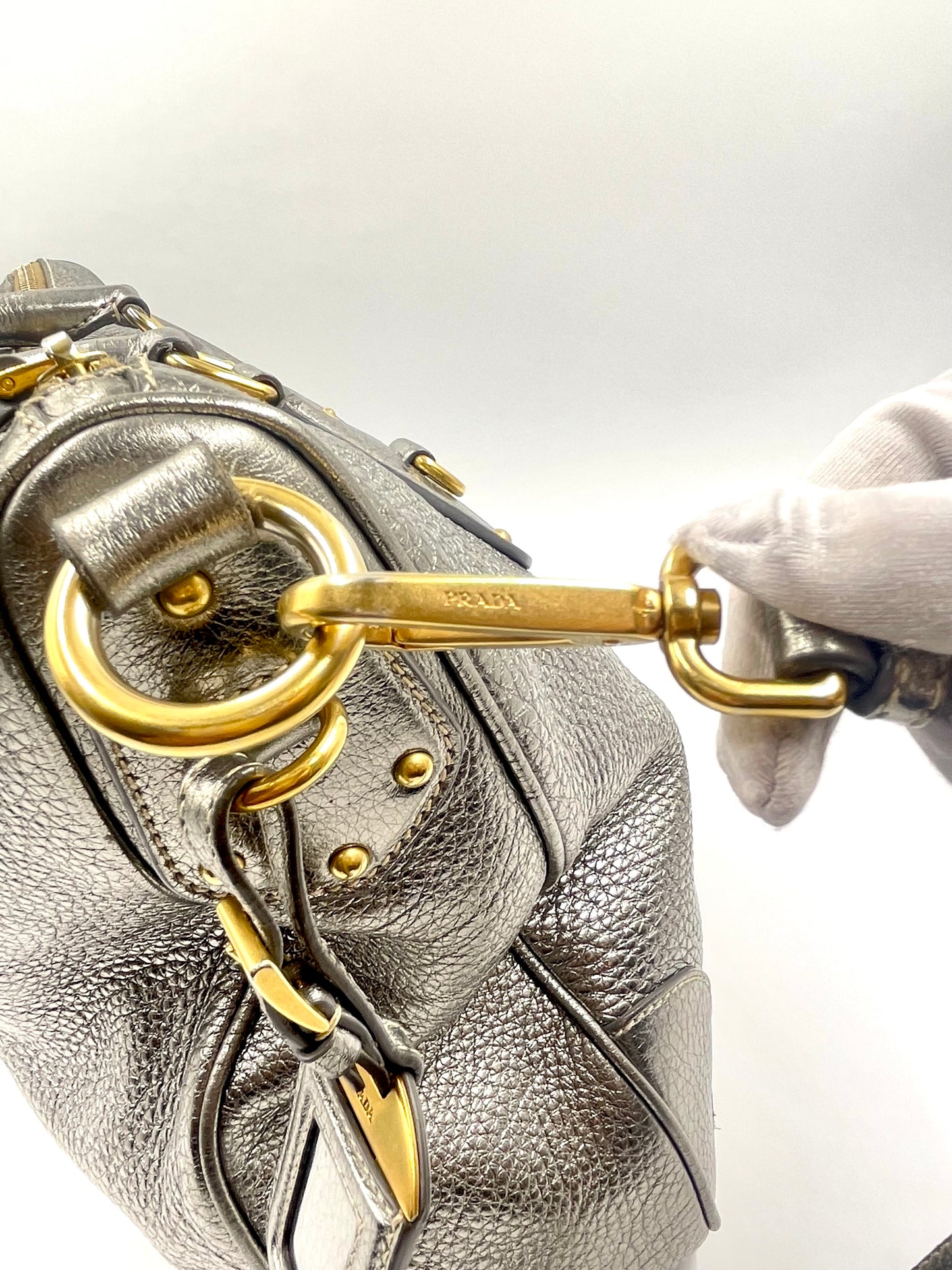 Prada Silver Metallic Vitello Daino Tote with gold-tone hardware and logo, held by a gloved hand.