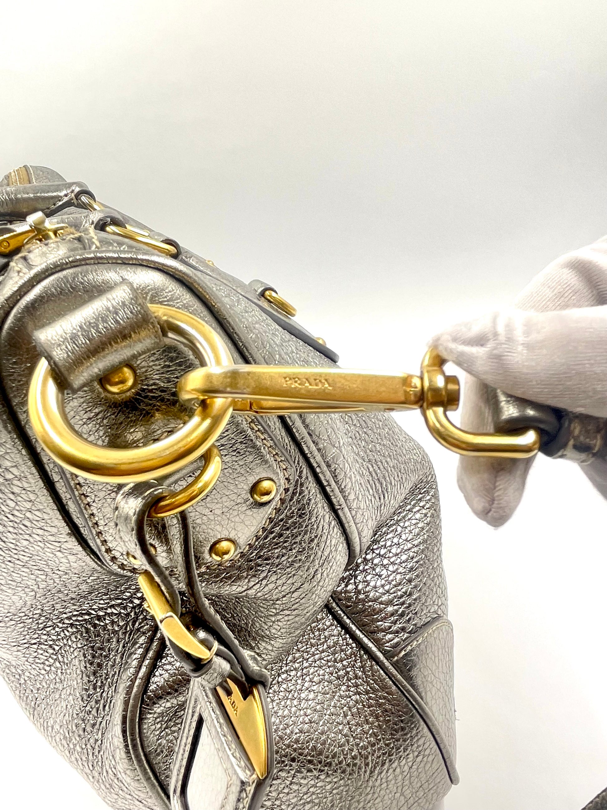 Prada Silver Metallic Vitello Daino Tote with gold-tone hardware and logo, held by a gloved hand.