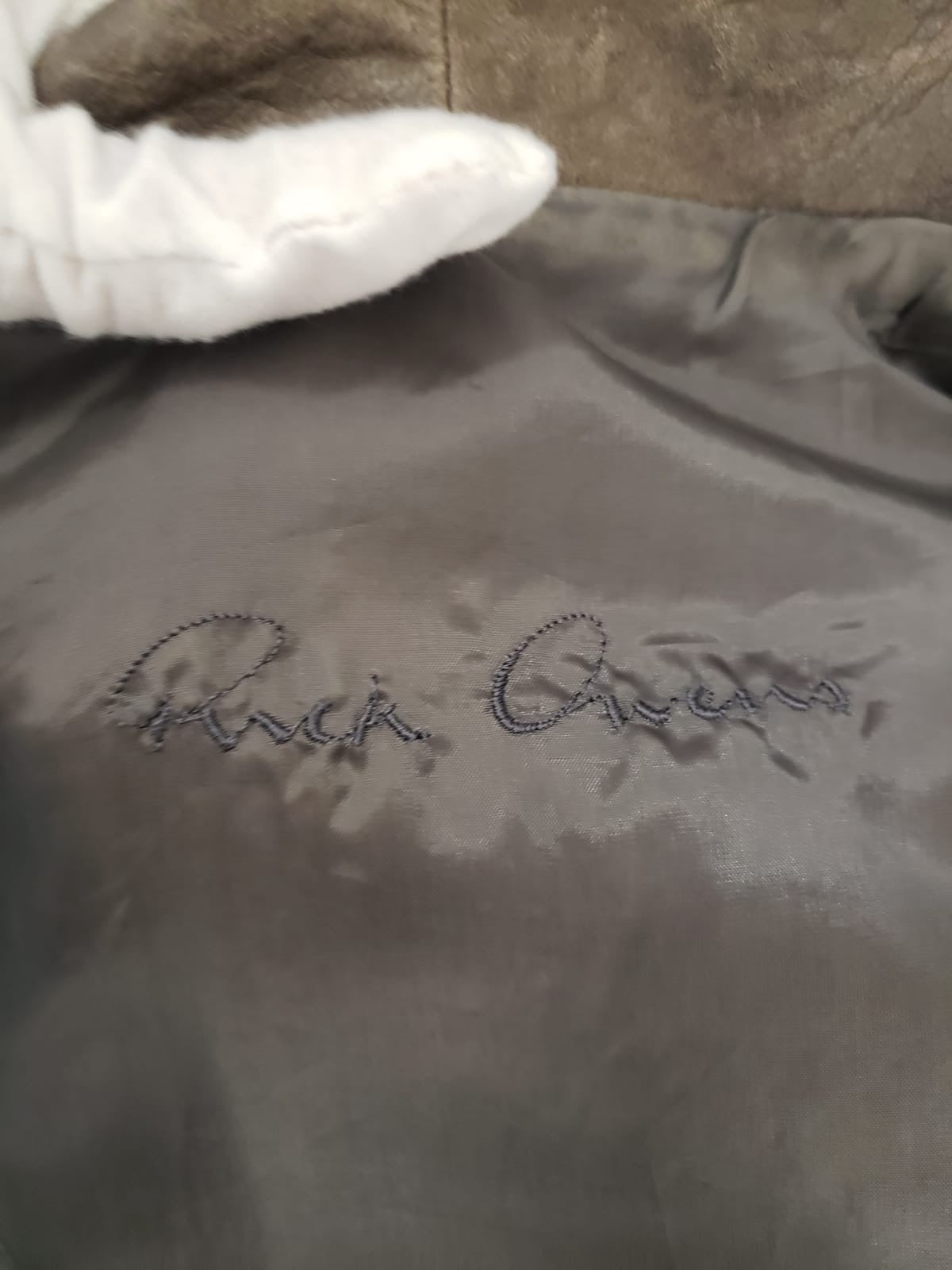 Close-up of the Rick Owens signature logo embroidered on the dark grey lining of a brown leather jacket.