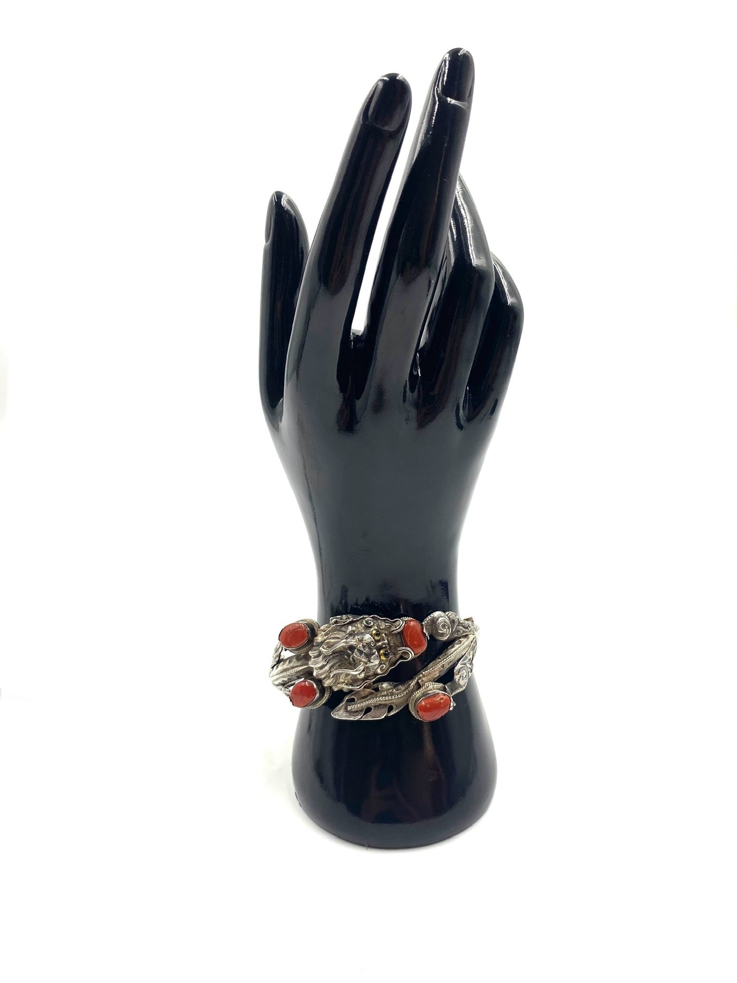 Sculpted sterling silver dragon bracelet with high-relief details and four red coral cabochons on a black display hand.