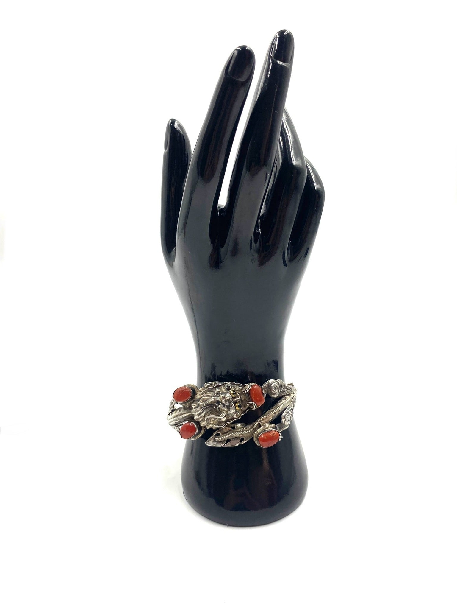 Sculpted sterling silver dragon bracelet with high-relief details and four red coral cabochons on a black display hand.