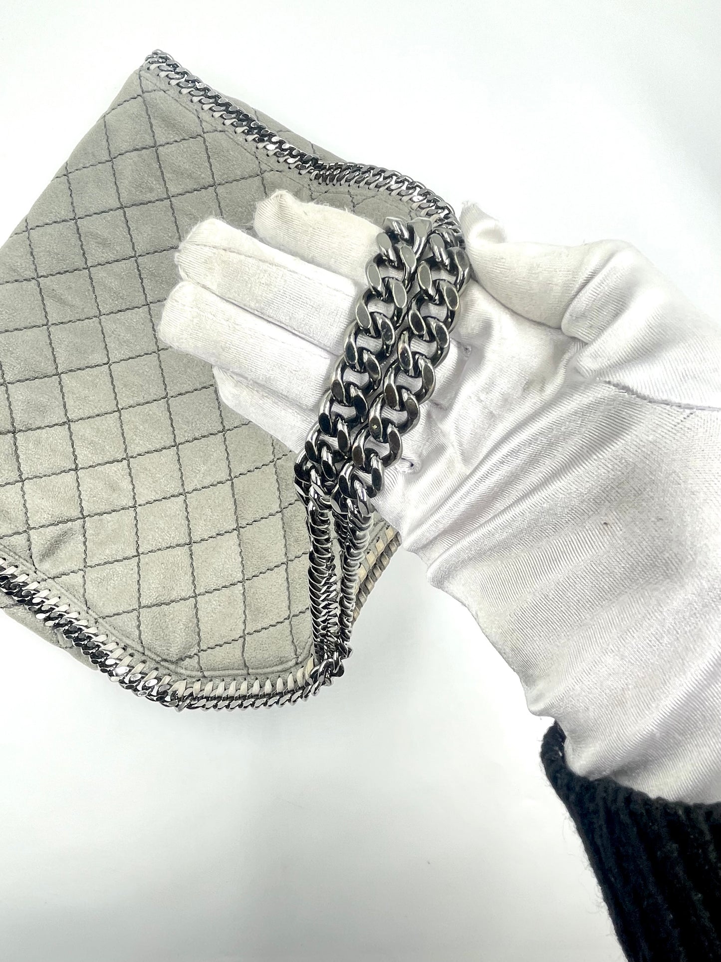 Hand holding a Stella McCartney Falabella grey quilted suede tote with silver chain strap.