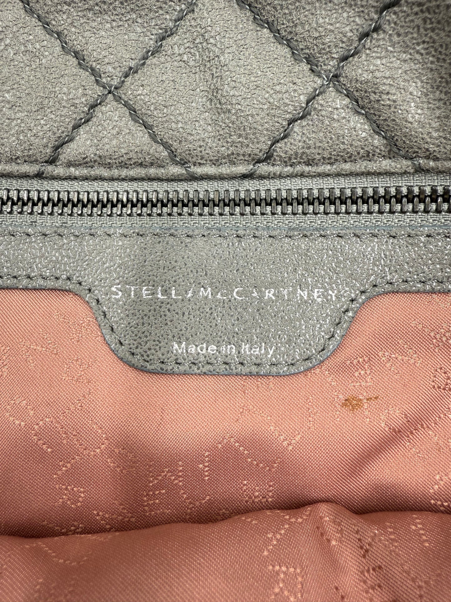 Close-up of Stella McCartney Falabella grey quilted suede bag interior with logo tag and zipper.