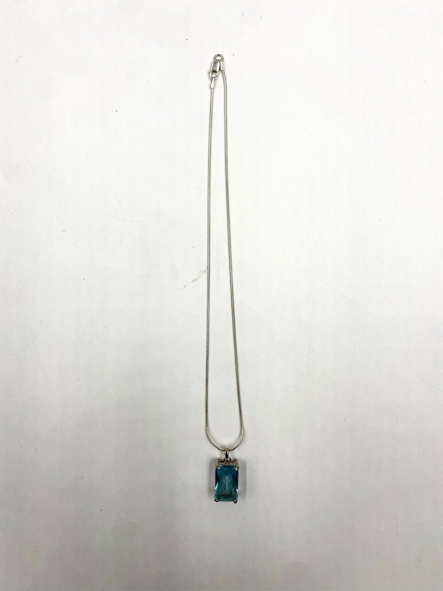 Sterling silver necklace with a rectangular blue topaz pendant on a white background.