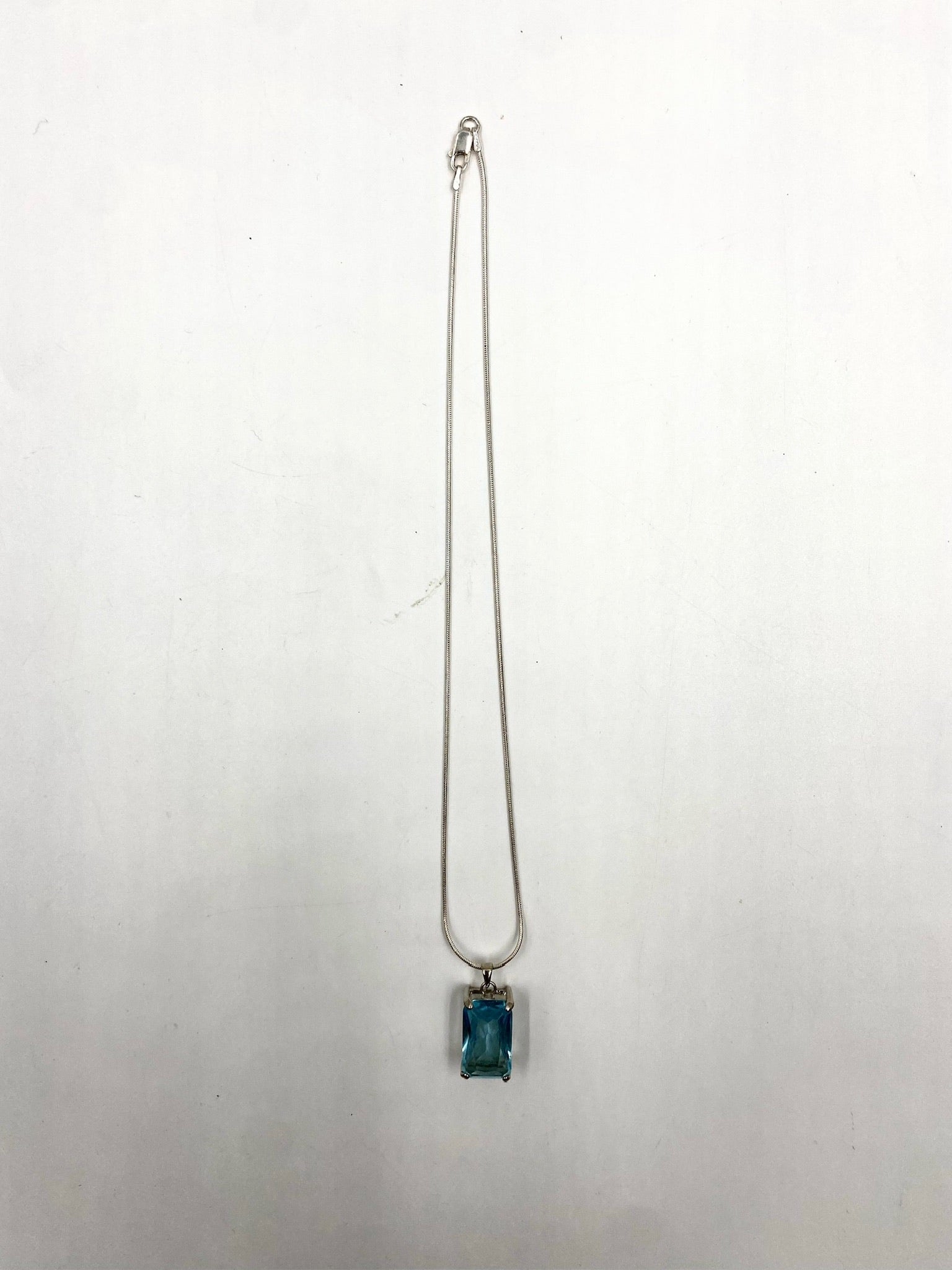 Sterling silver necklace with a rectangular blue topaz pendant on a white background.