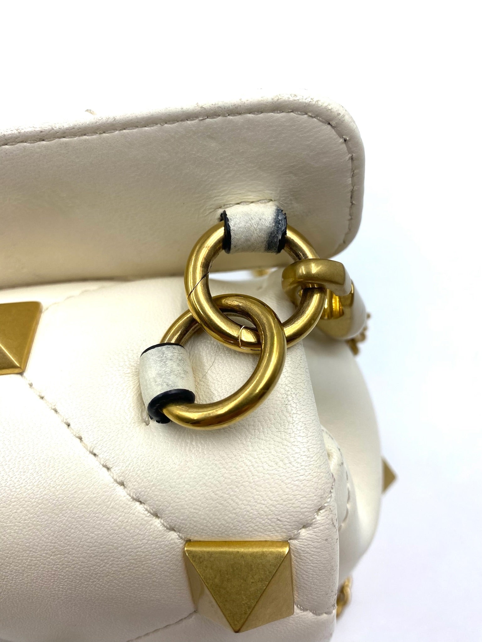Close-up of a white Valentino Garavani Roman Stud bag showing wear on the strap attachment and gold hardware.