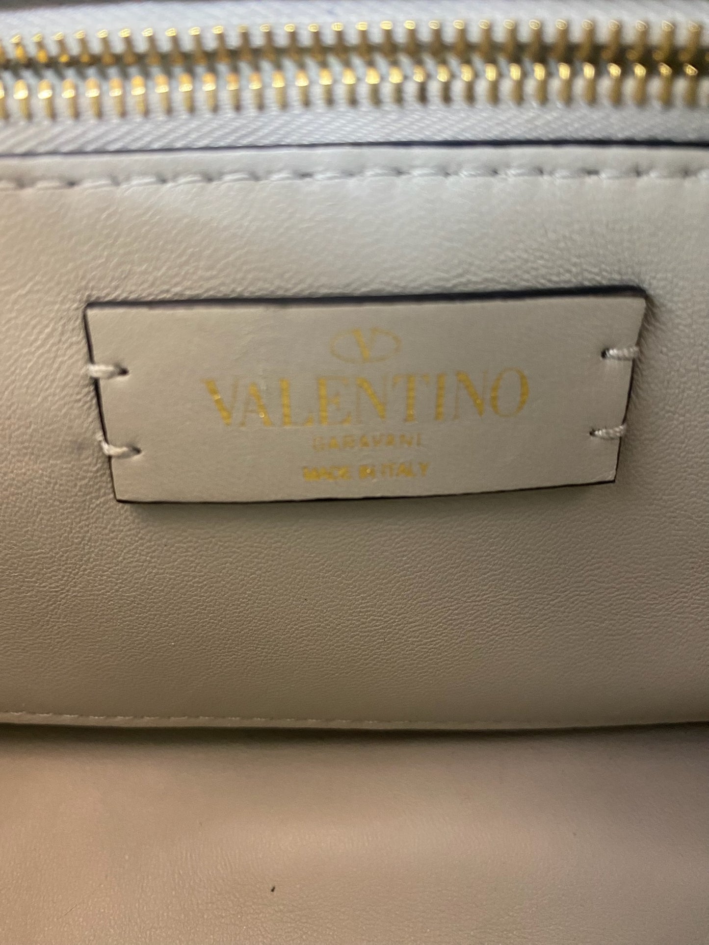 Close-up of the gold Valentino Garavani logo on a white leather bag.