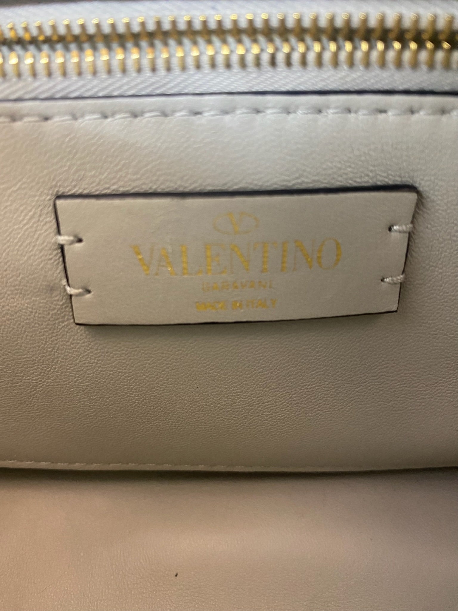 Close-up of the gold Valentino Garavani logo on a white leather bag.