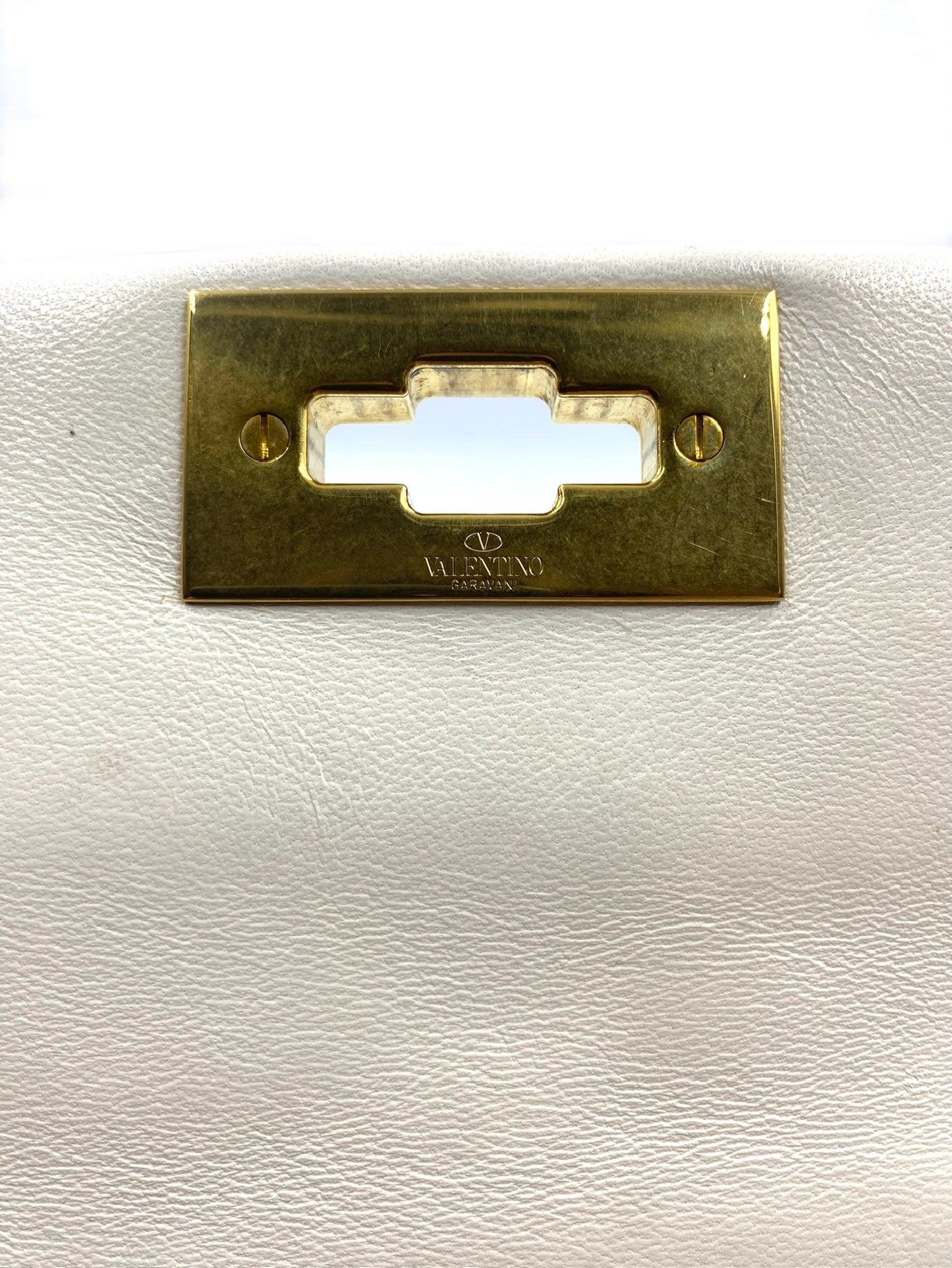 Close-up of Valentino Garavani white leather Roman Stud bag's gold clasp with logo.