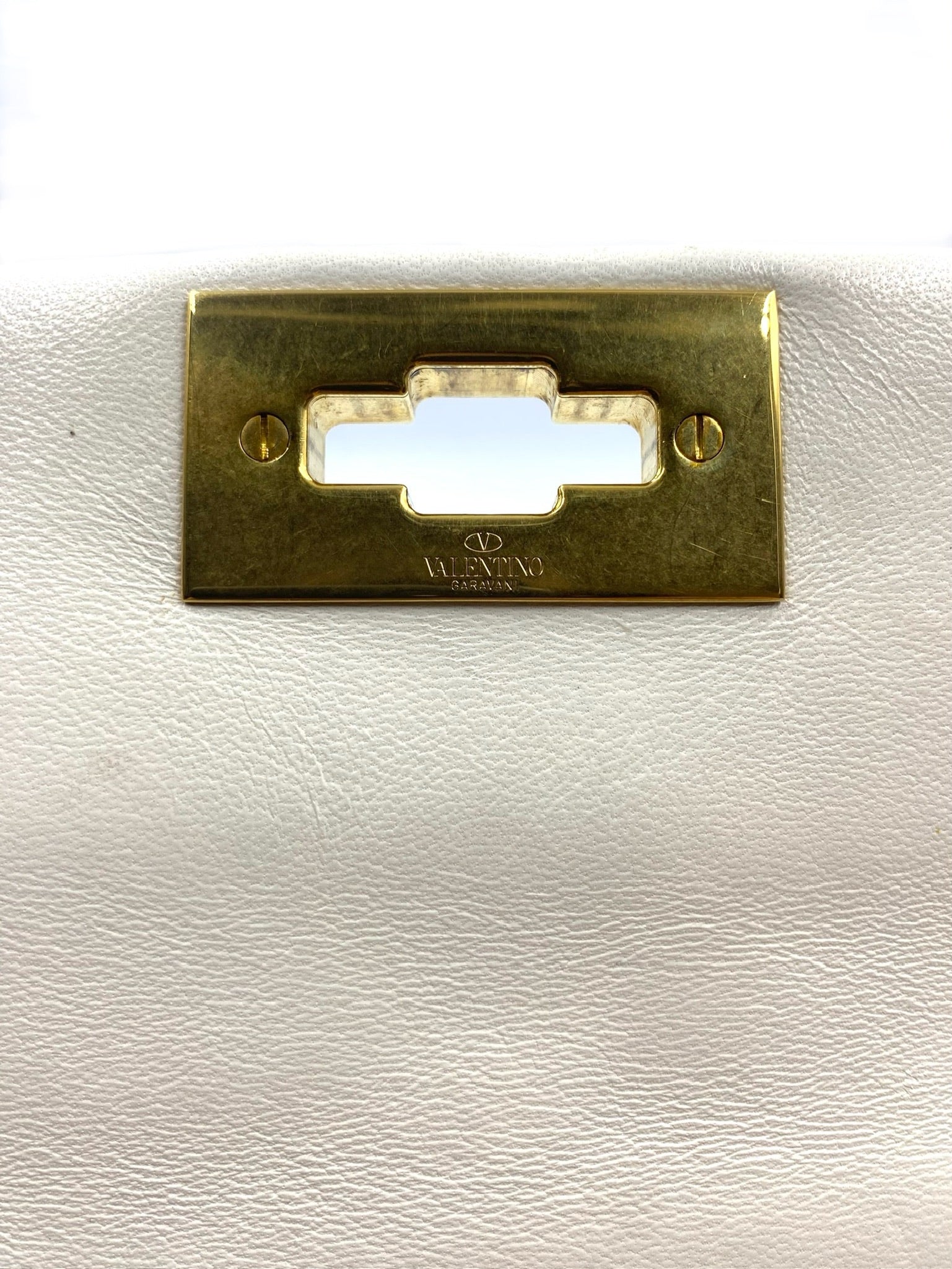 Close-up of Valentino Garavani white leather Roman Stud bag's gold clasp with logo.