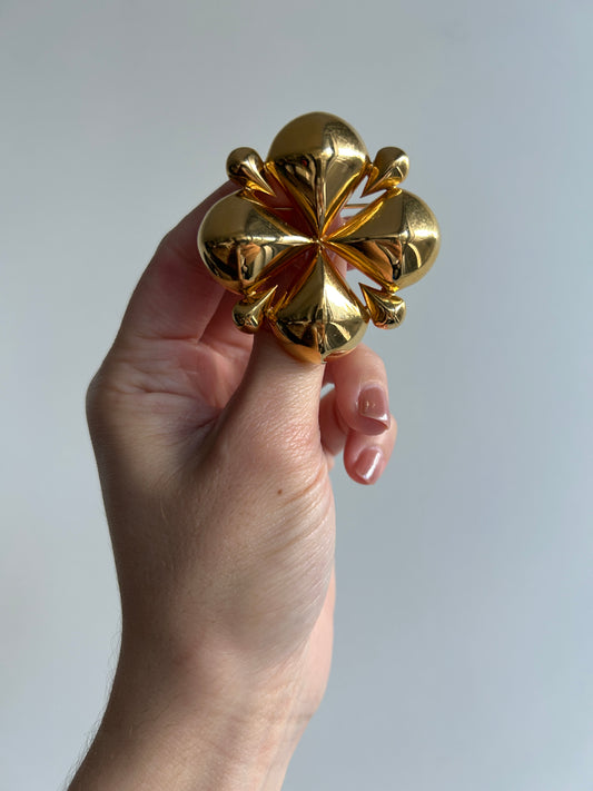 Hand holding a vintage 1980s Monet clover brooch, gold-toned with a shiny, dimensional design.