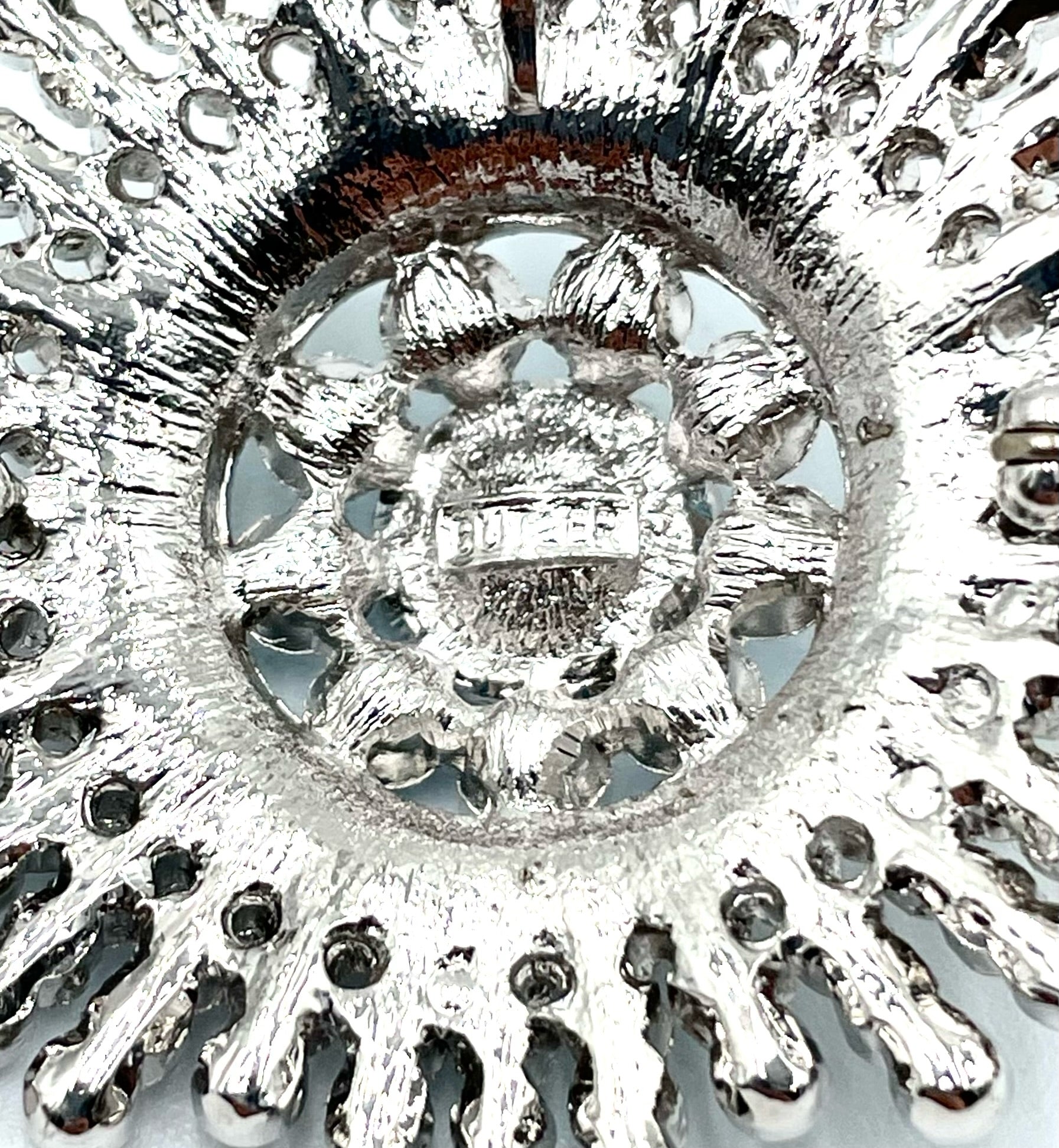 Back of a silver-toned Butler sunburst brooch with intricate metalwork and a pin clasp.