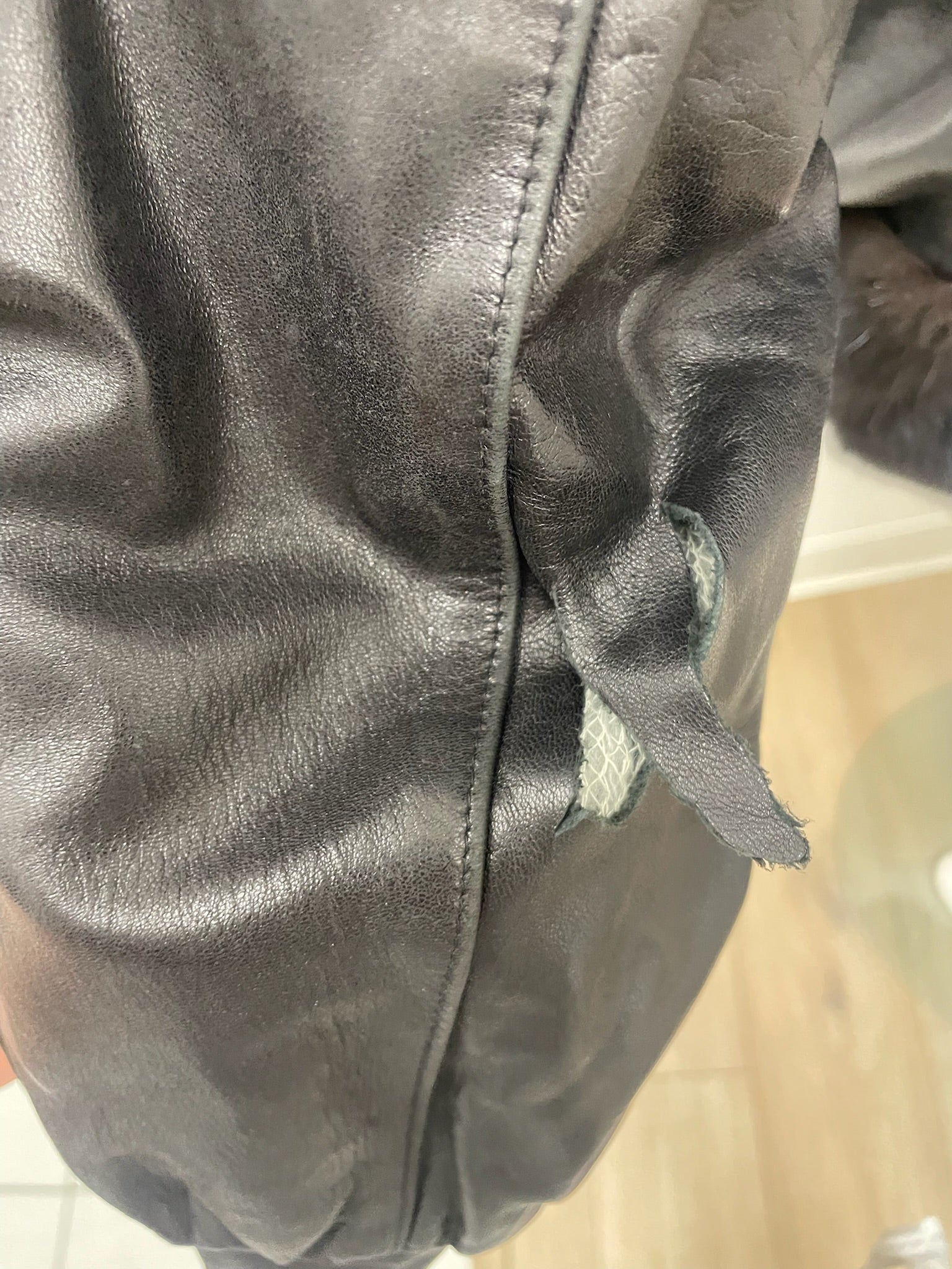 Close-up of a black vintage leather jacket sleeve showing a visible tear in the material.