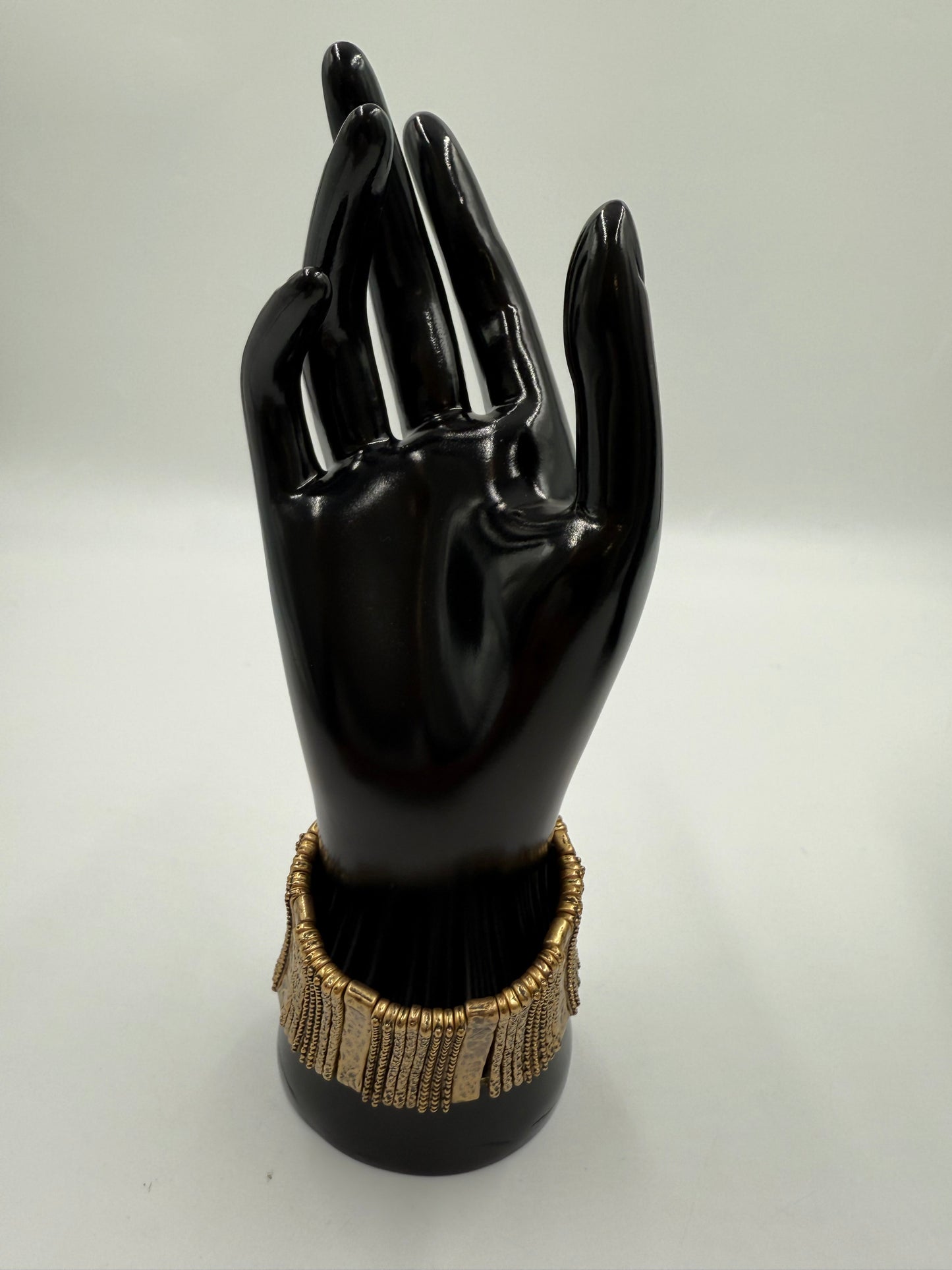 Vintage gold-tone costume jewelry stretch bracelet with textured rectangular links on a black display hand.