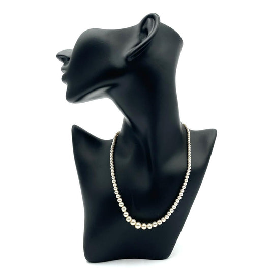 Vintage pearl necklace with graduating ivory-toned pearls and a silver-tone clasp on a black mannequin.