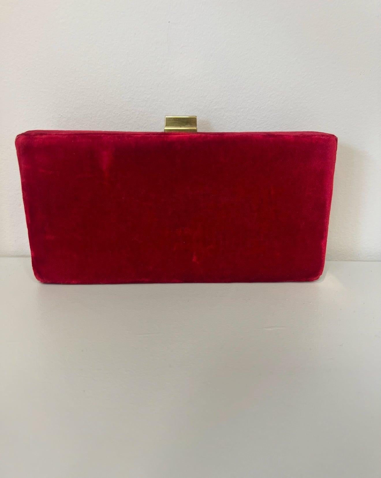 Rectangular red velvet clutch with a minimalist gold metal clasp closure, set against a plain white background.