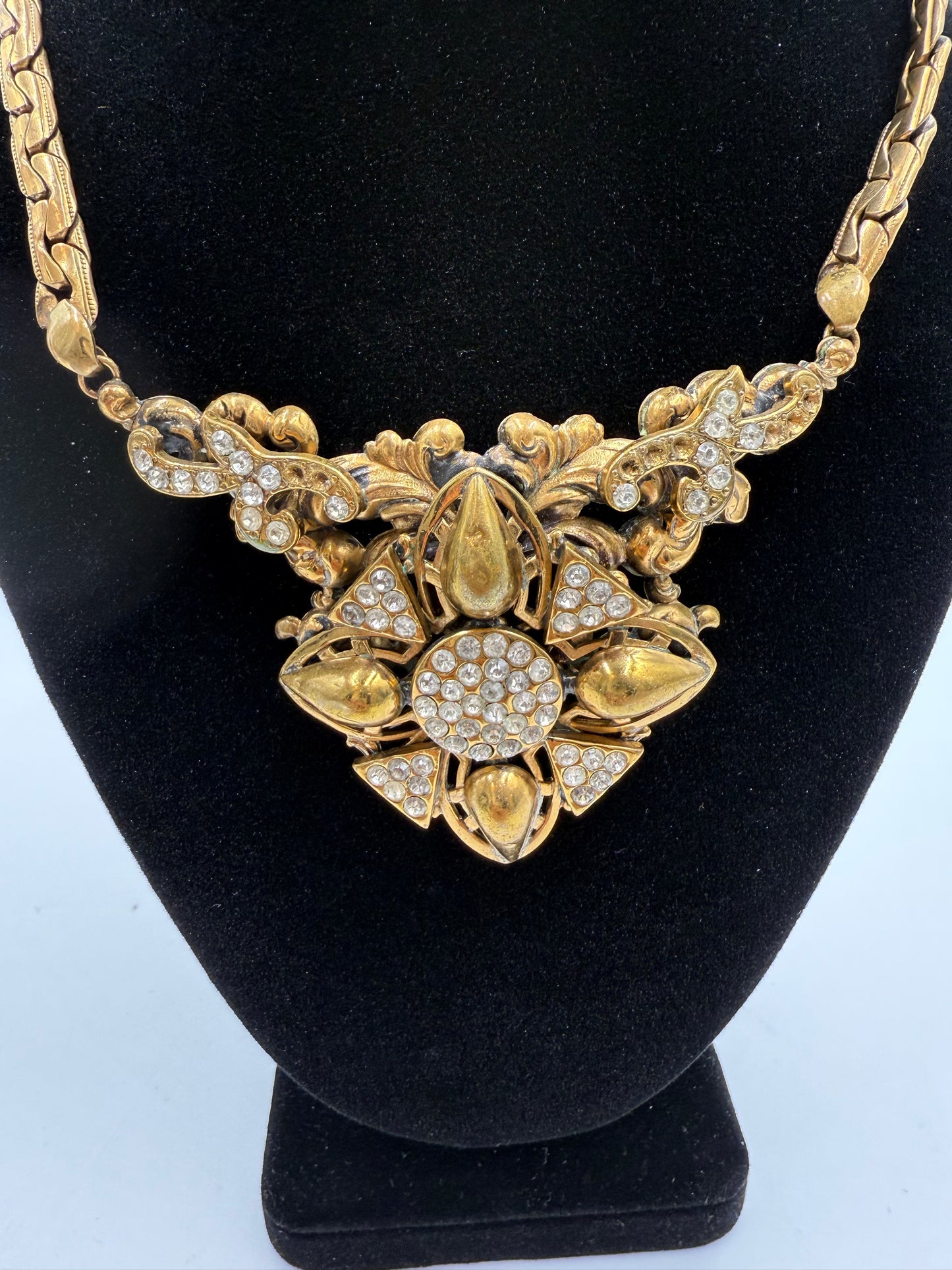 Vintage gold plated bib necklace with intricate floral design and clear rhinestones on a black display.