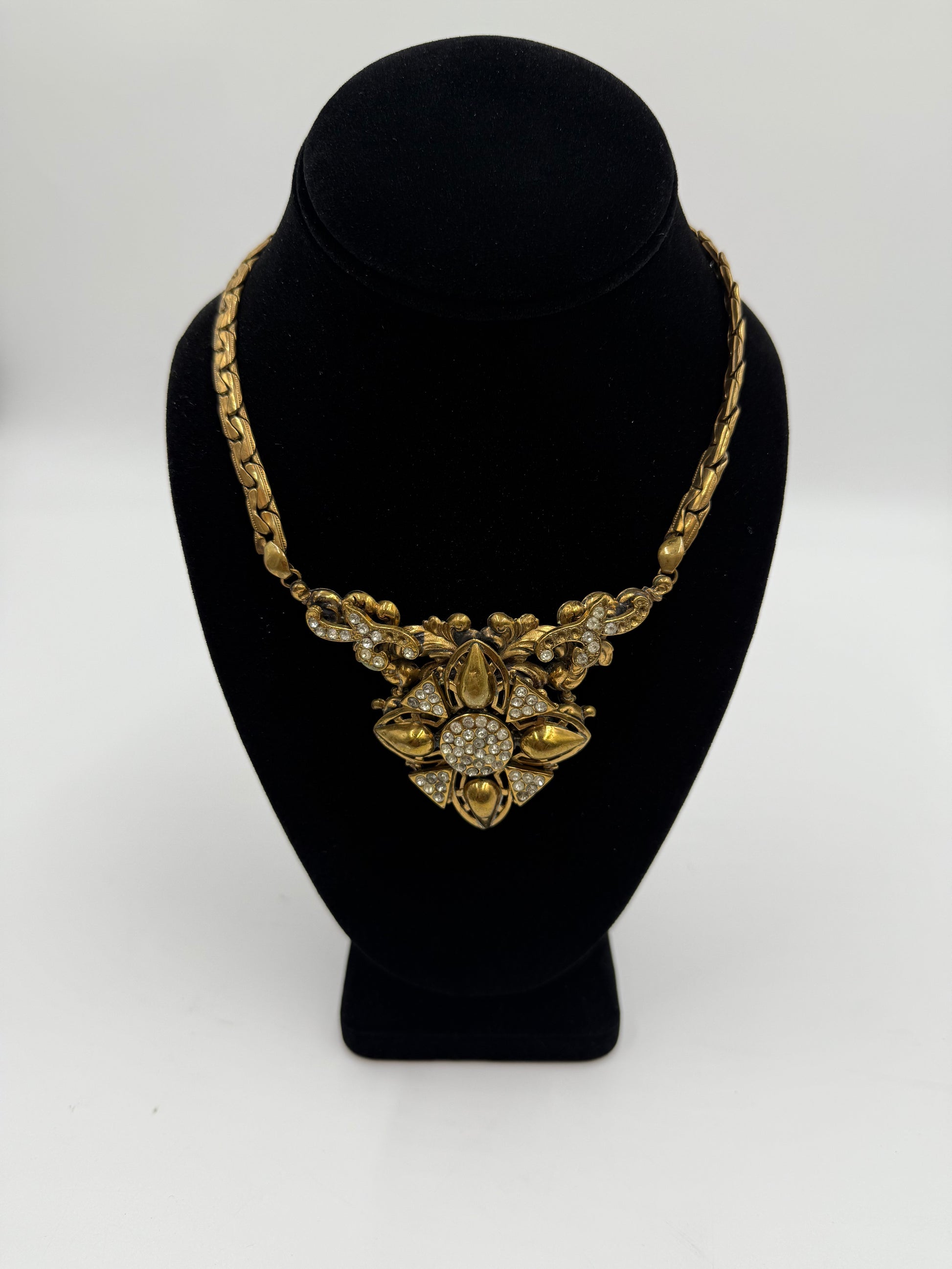 Vintage gold plated bib necklace with rhinestone details on a black display.