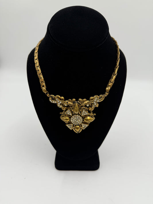 Vintage gold plated bib necklace with rhinestone details on a black display.