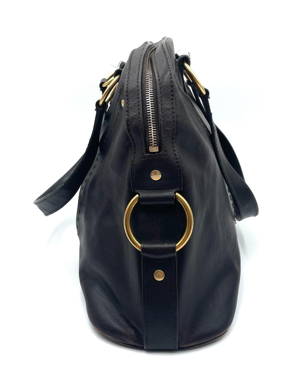 Side view of a dark brown leather Yves Saint Laurent Muse bag with gold-tone hardware, ring details, and a zip closure.