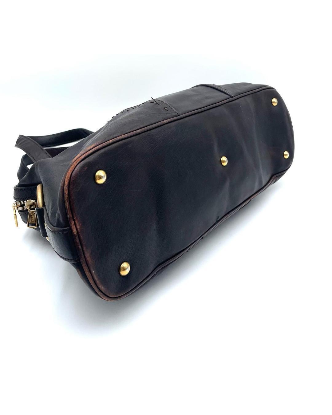 Bottom view of a dark brown leather Yves Saint Laurent Muse bag with gold-tone feet and visible corner wear.