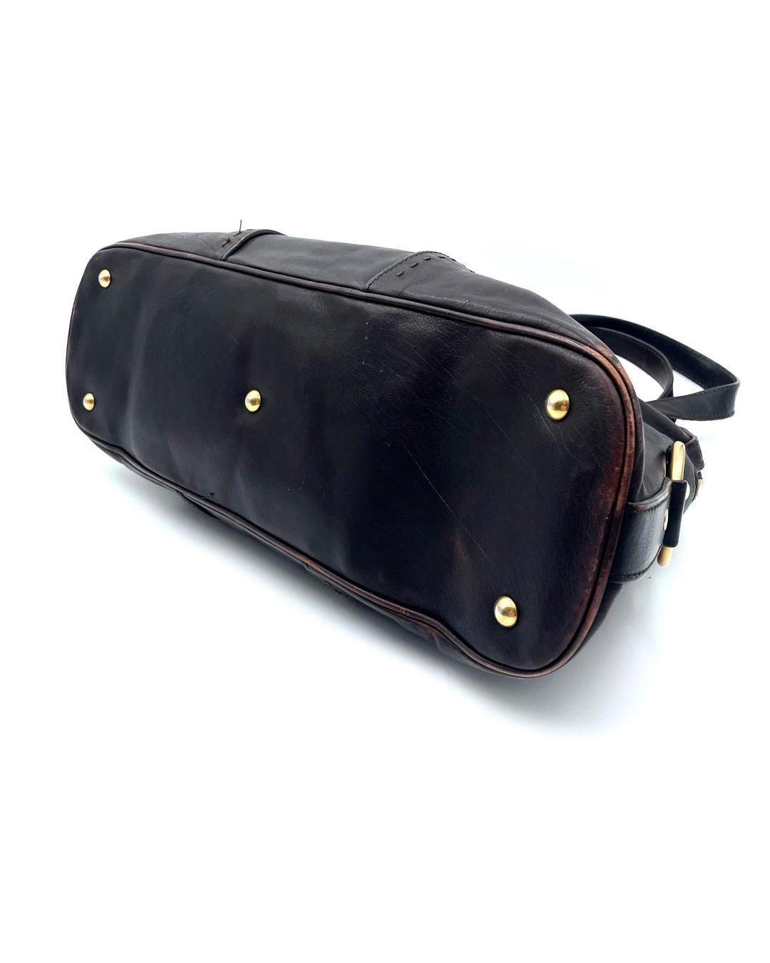 Bottom view of a dark brown leather Yves Saint Laurent Muse bag with gold-tone protective feet and visible corner wear.