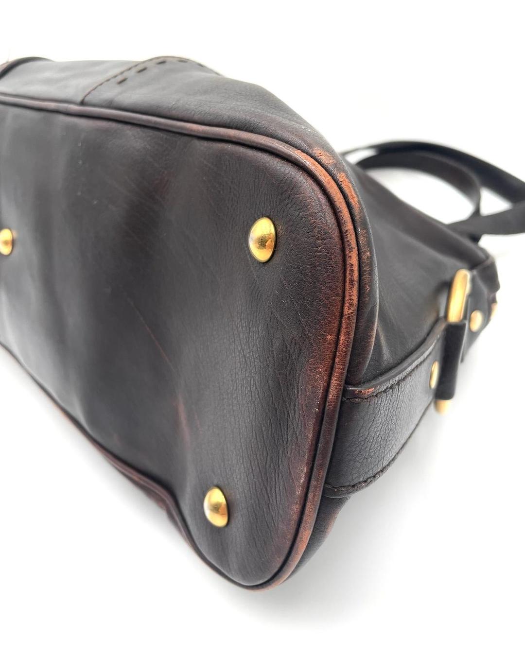 Bottom view of a dark brown leather YSL Muse bag showing gold-tone feet and visible corner wear.