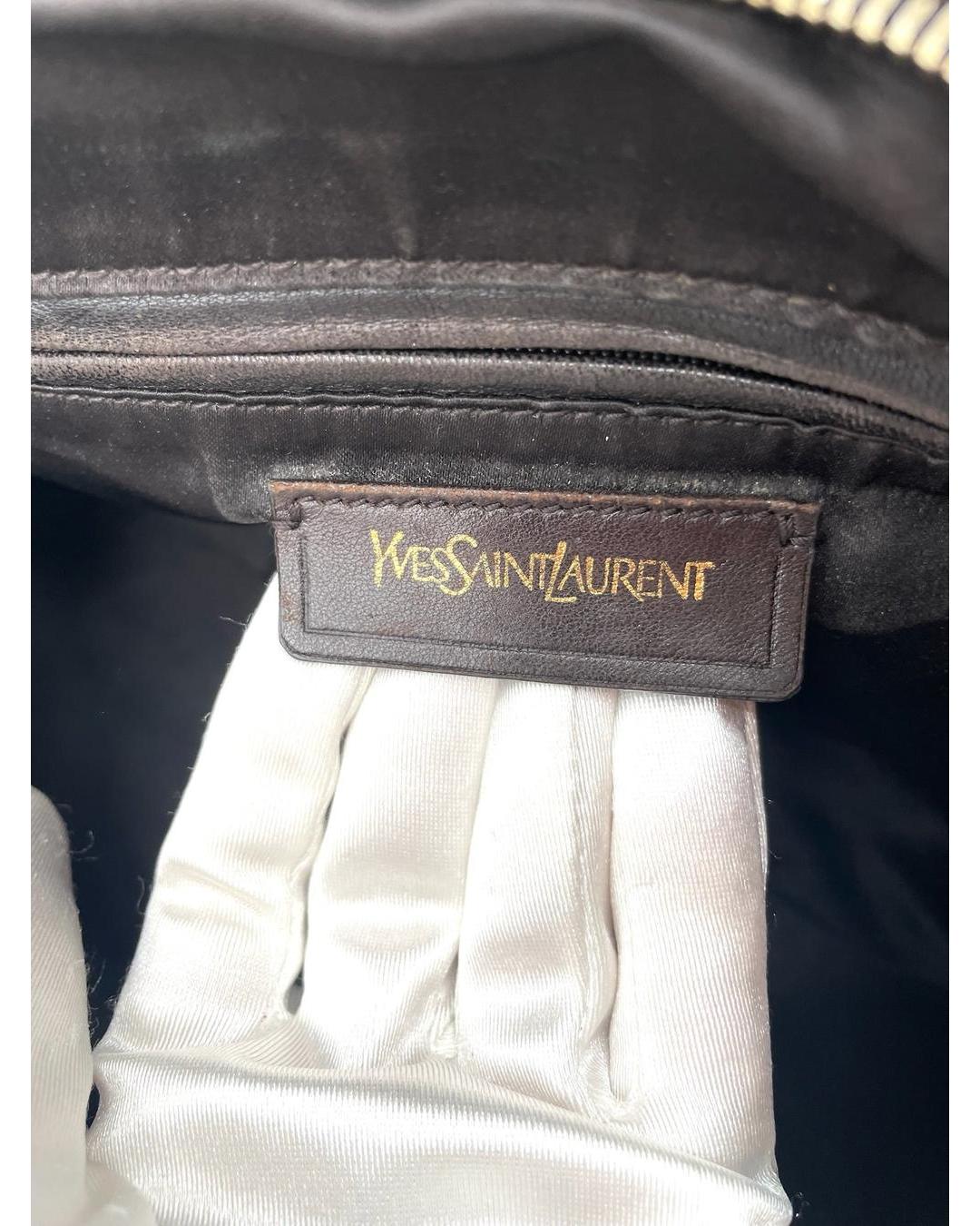 Dark brown leather Yves Saint Laurent Muse bag interior label with gold embossed logo held by a gloved hand.